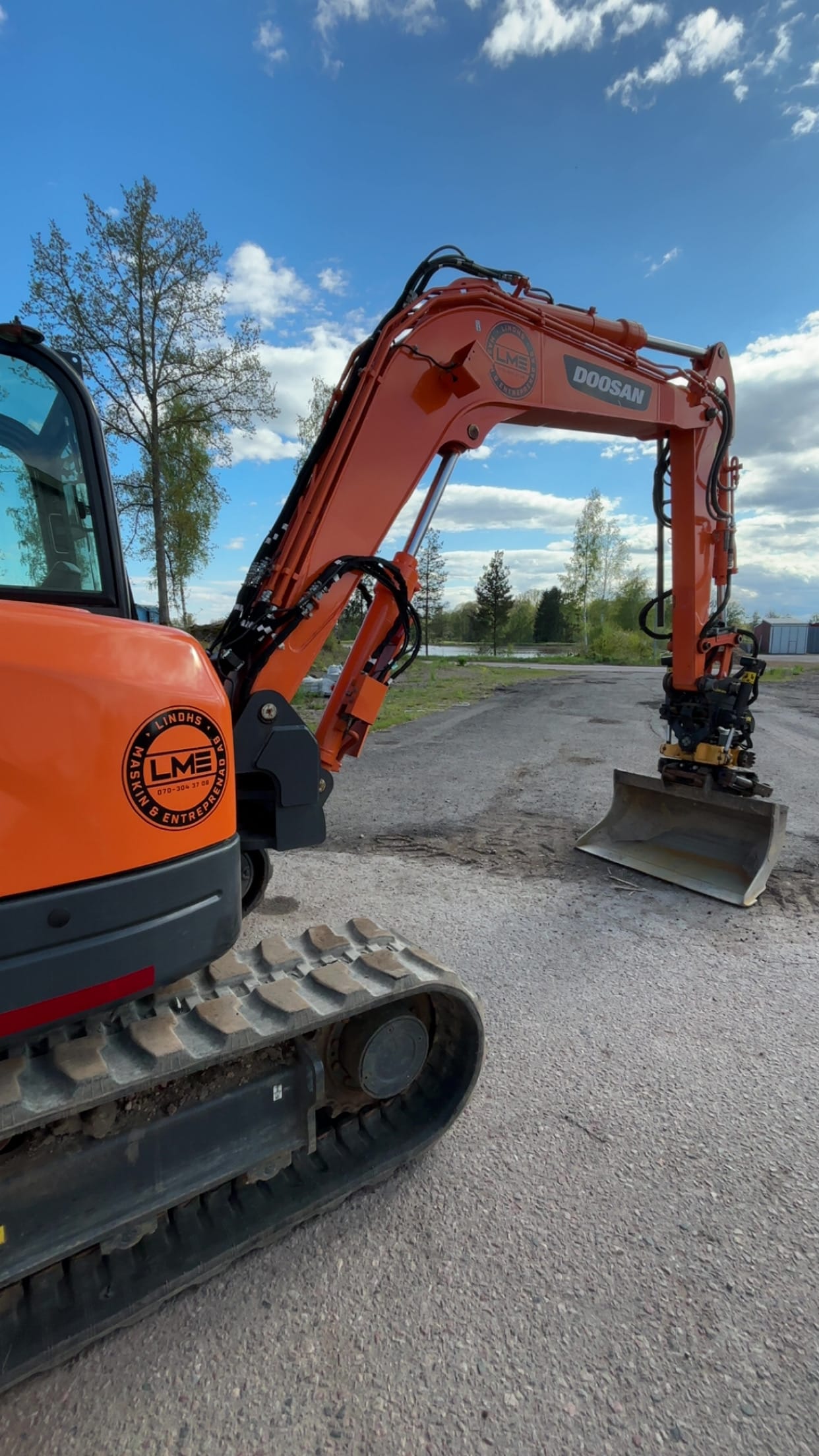 Orange Doosan-grävmaskin med LME-logotyp och släntskopa på grusplan