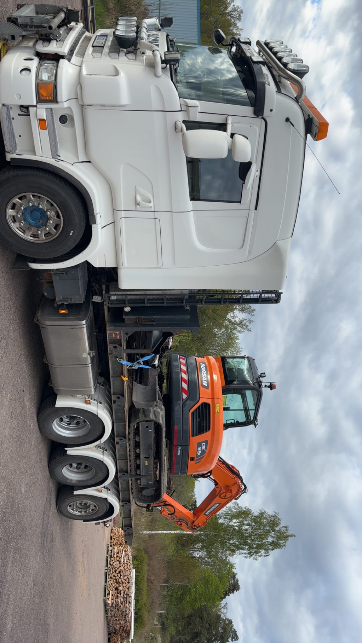 Vit lastbil med orange Doosan-grävmaskin på släp